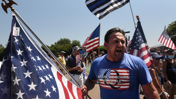 Un homme brandissant un drapeau américain porte un tee-shirt à l'effigie de QAnon.