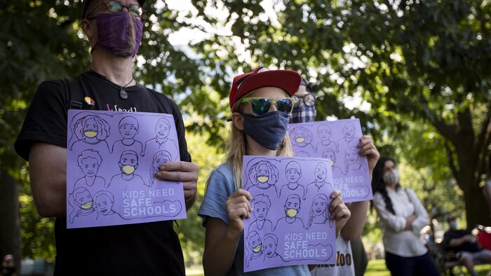 Un enfant et un adulte sont dans un parc. Ils sont masqués et ont dans les mains une affiche.