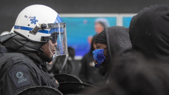 Un manifestant est face-à-face avec un policier en tenue antiémeute.