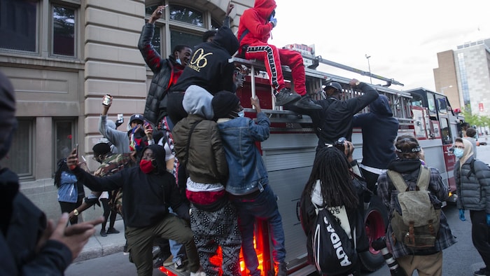 Plusieurs manifestants sur un camion de pompier qui roule dans le centre-ville de Montréal.