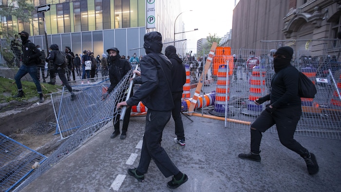 Des manifestants déplacent des clôtures de sécurité et des cônes routiers au centre-ville de Montréal.