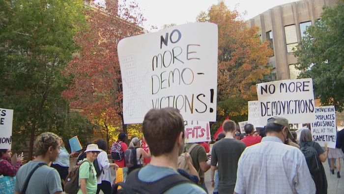 Un groupe de personnes marchent avec des pancartes demandant la fin des réno-évictions.