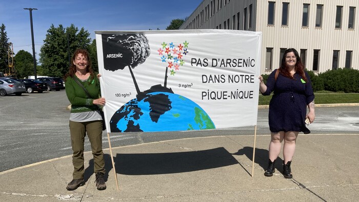 Deux femmes tiennent une banderole mentionnant « Pas d'arsenic dans notre pique-nique ».