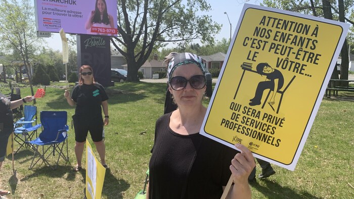 Une femme tient une affiche qui indique «Attention à nos enfants c'est peut-être le vôtre... qui sera privé de services professionnels». 