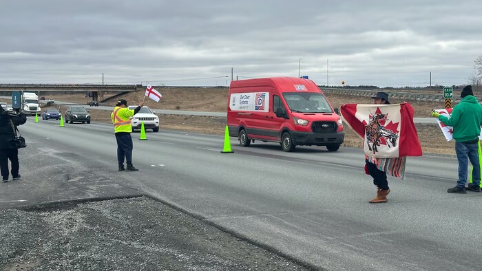 Des manifestants sur la route agitent des drapeaux.