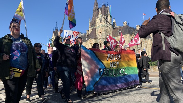 Des manifestants marchent derrière le drapeau LGBTQ+.