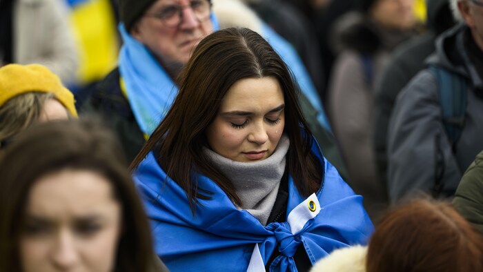 Entourée d'une foule, une femme drapée dans un drapeau ukrainien verse une larme.