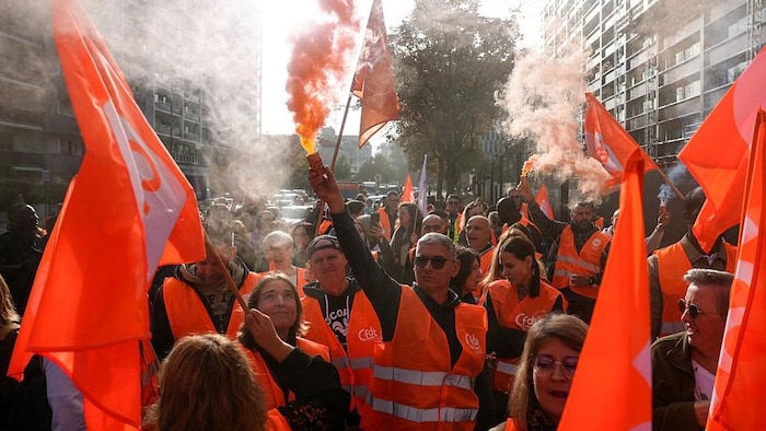 Une foule de manifestantes et de manifestants, arborant des vestes réfléchissantes, des drapeaux et des tubes de fumée colorées manifestent dehors.