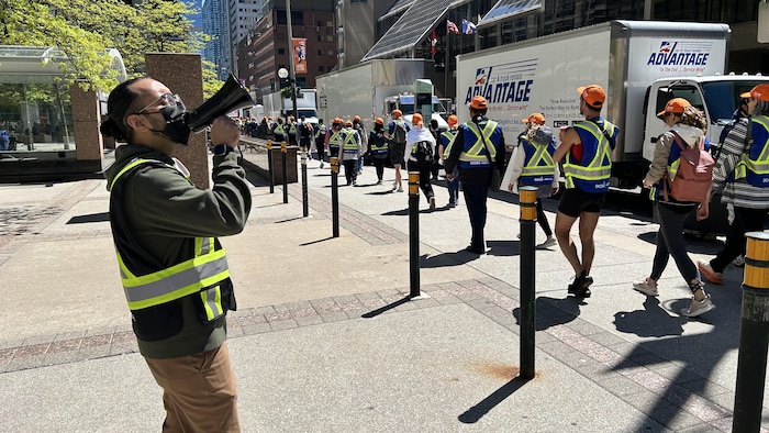 Une personne avec un mégaphone et un gilet de sécurité, le 26 mai 2025 à Toronto.