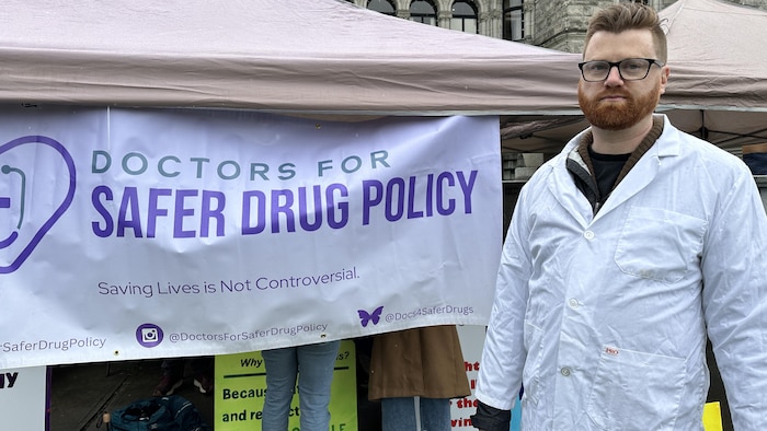 Ryan Herriot devant une banderole de l'organisme Doctors fo safer drug policy.