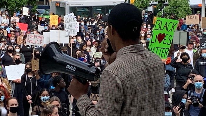 Un homme fait un discours devant de centaines de manifestants réunis devant le Musée des beaux-arts de Vancouver.