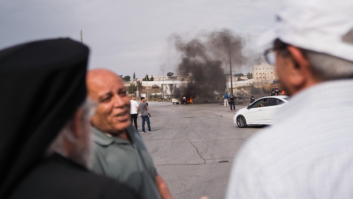 Trois hommes discutent calmement à une centaine de mètres de pneus qui brûlent.
