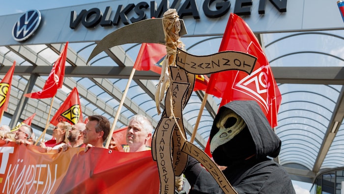 Des manifestants tiennent des drapeaux et des banderoles; l'un d'entre eux est costumé en faucheuse.