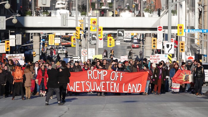 Des manifestants marchant derrière une bannière dans la rue Wellington, à Ottawa, en hiver.