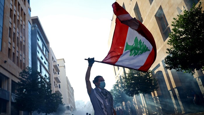 Un homme portant un masque chirurgical brandit un grand drapeau du Liban.