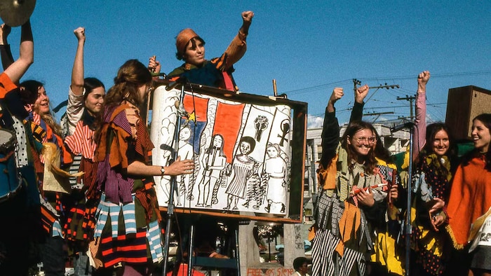 Des jeunes qui manifestent les poun levés vers le ciel et des pancartes qui symbolisent l'égalité pour les femmes. 
