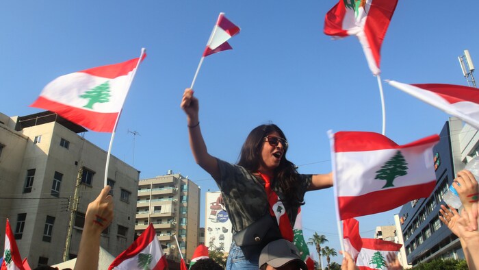 Une manifestantes se tient sur les épaules d'un homme, brandissant des drapeaux libanais à Sidon, le 19 octobre 2019. 