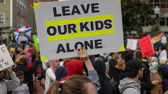 Une main tenant une affiche sur laquelle il est écrit: "Laissez nos enfants tranquilles". 