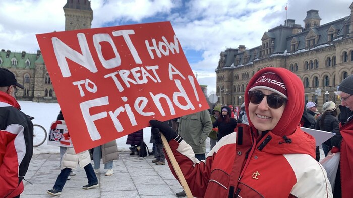 Une femme tient une pancarte sur laquelle il est inscrit en anglais : ce n'est pas la façon dont on traite un ami.