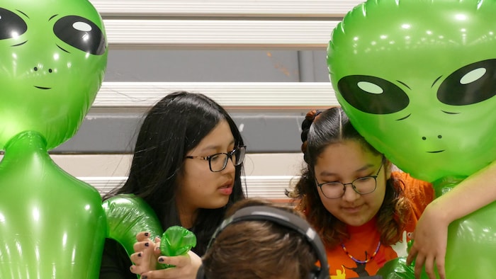 Deux jeunes filles entourées d’extraterrestres gonflables. 
