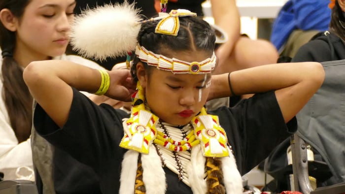 Une jeune danseuse autochtone attache sa coiffe.
