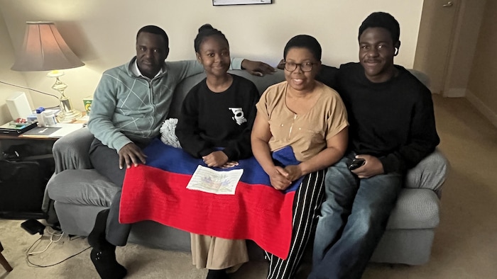 Quatre personnes assises sur un fauteuil avec un drapeau haïtien sur les genoux.