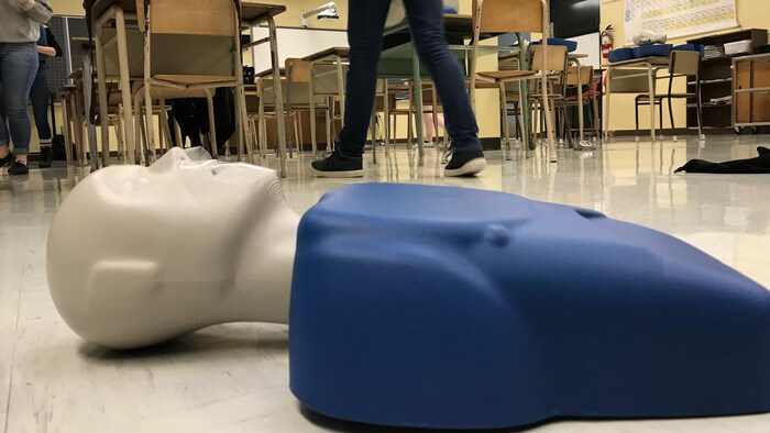 Un mannequin pour pratiquer la réanimation cardiaque est étendu sur le plancher d'une salle de classe.