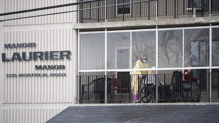Un travailleur qui porte de l'équipement de protection s'occupe de résidents sur un balcon du Manoir Laurier, à Ottawa.