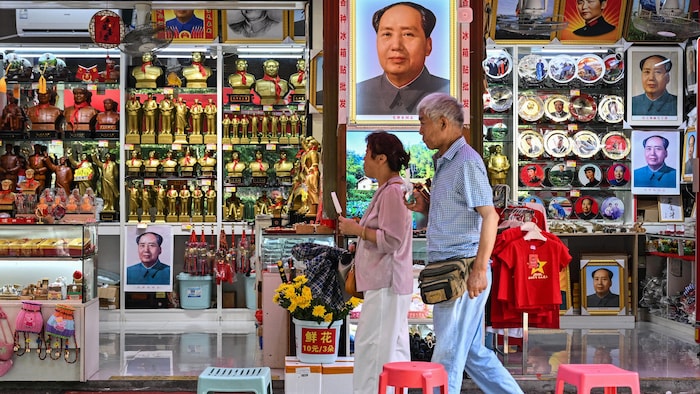 deux personnes passent devant une boutique remplie de produits colorés à l'effigie de Mao.