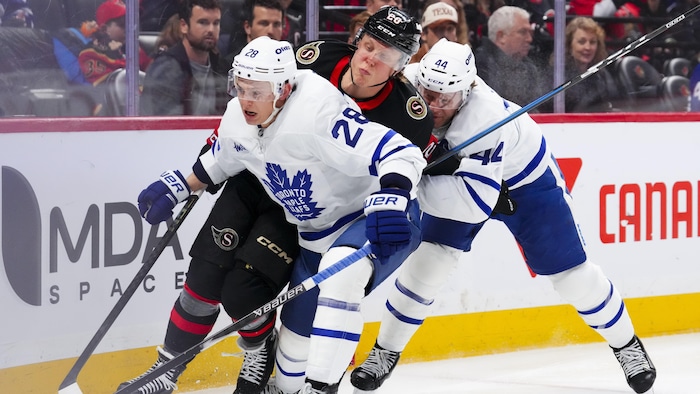 Deux joueurs des Maple Leafs luttent avec un joueur des Sénateurs pour la rondelle. 