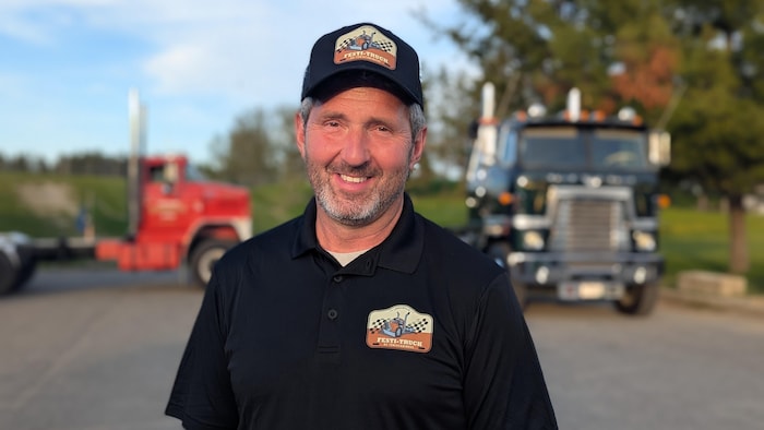 Marc Bernard pose dans une cour avec deux camions derrière.