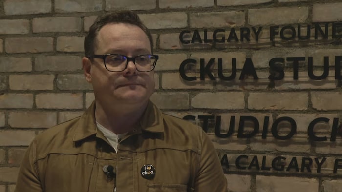 Un homme avec des lunettes porte un macaron qui dit "J'aime CKUA". 