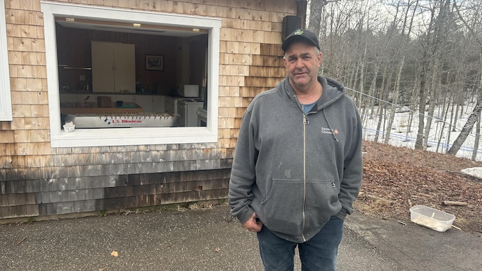 Marc Chiasson debout devant la cabane à sucre, avec des érables en arrière.