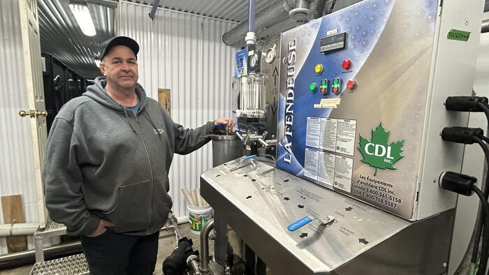 Un homme dans son érablière devant un concentrateur en acier inoxydable.