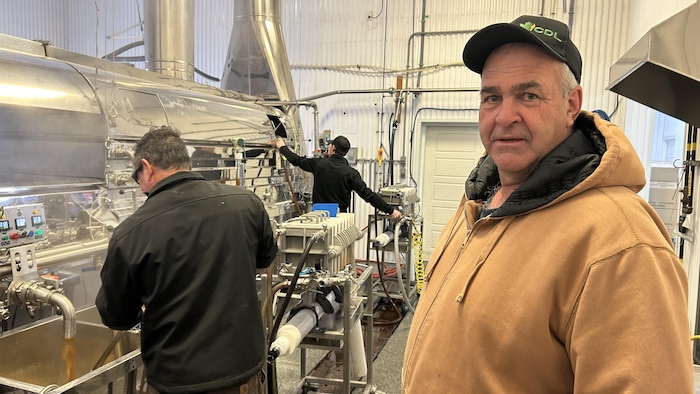 Marc Chiasson regarde la caméra, des employés à côté de lui dans une salle de transformation de l'eau d'érable.