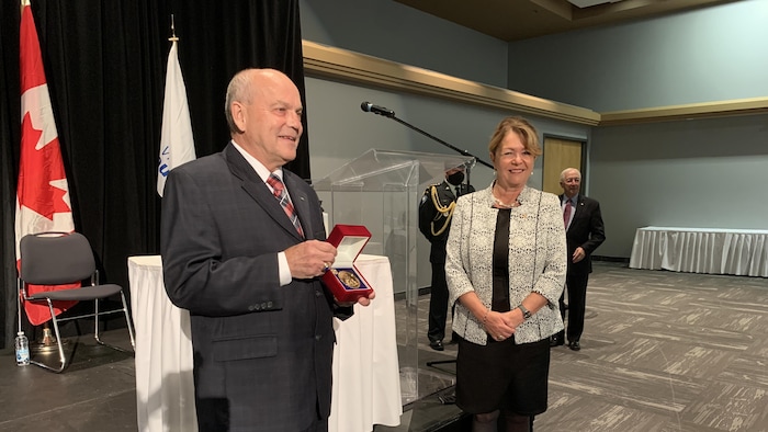 Marc Lemay montre sa médaille aux gens dans la salle. La mairesse de Rouyn-Noranda, Diane Dallaire, sourit aussi.