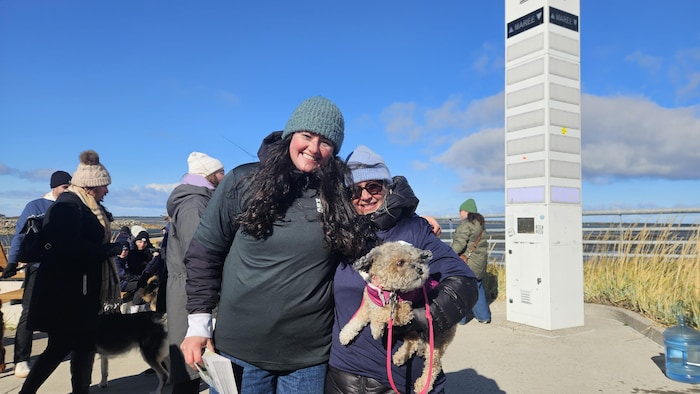 Deux femmes sourient à la caméra. L'une d'elles a un chien dans ses bras. 