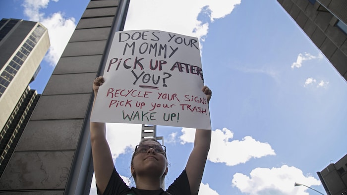 Une manifestante porte une pancarte où il est inscrit : « Does your mommy pick up after you ? Recycle your signs, pick up your trash. wake up! »