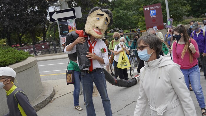 Des manifestants marchent dans la rue. Parmi eux, une caricature en papier mâché du premier ministre canadien, Justin Trudeau.