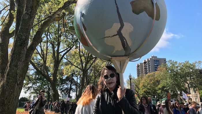 Une manifestante maquillée tient en main un immense globe terrestre.