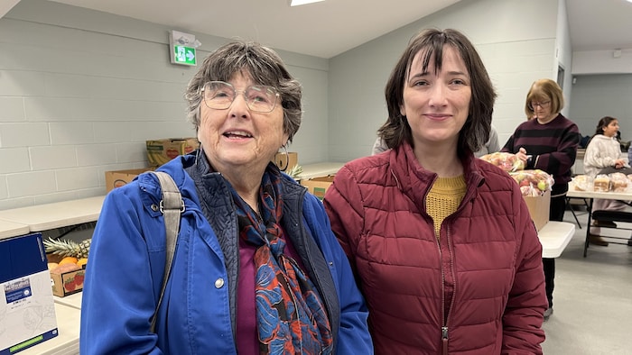 Deux femmes font la pose devant des boîtes de carton remplies de fruits et de légumes. 