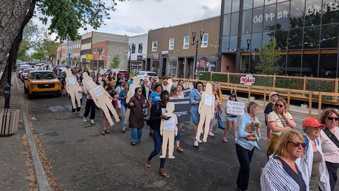 Un groupe de personnes marchant avec des affiches et des silhouettes de carton.