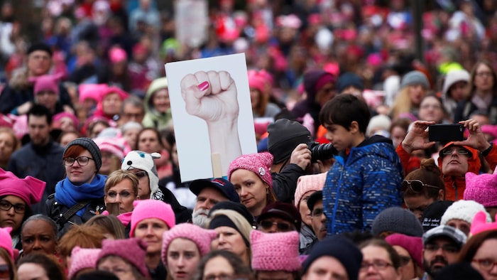 Une manifestante brandit une pancarte montrant un poing féminin levé et plusieurs autres portent un « Pussyhat », un chapeau en laine rose avec des oreilles de chat, en référence à des propos de Donald Trump diffusés pendant la campagne présidentielle.