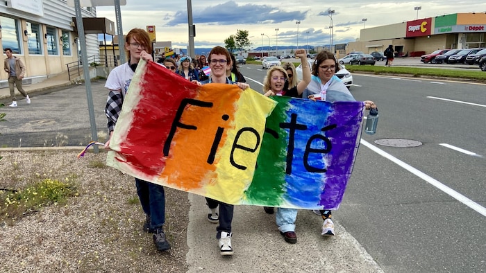 Quatre personnes marchent et tiennent un très grand drapeau de la fierté.