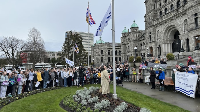 Une personne hisse un drapeau devant des gens rassemblés en cercle.