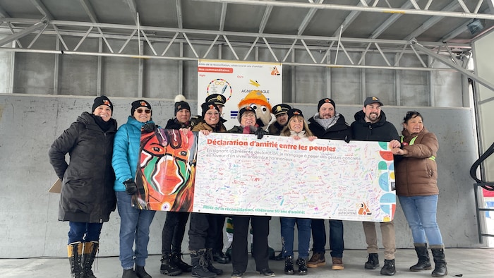 Plusieurs personnes tiennent une grande affiche en main pour la montrer au public. 