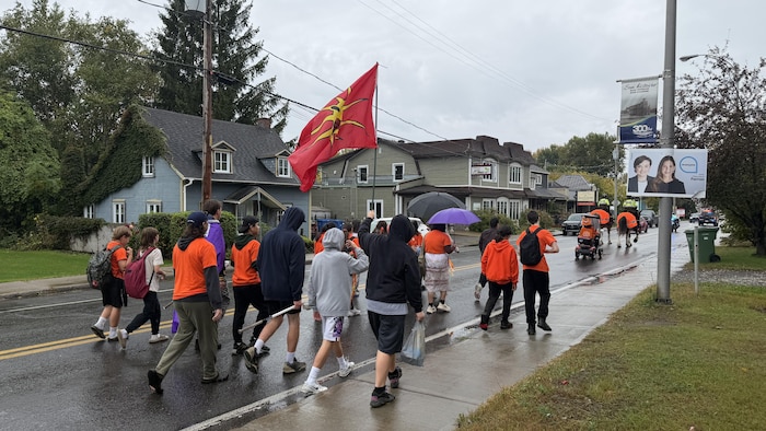 Des jeunes de dos marchent sur la route d'un village.