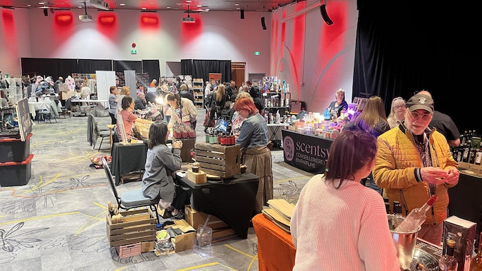 Plusieurs tables avec des artisans qui présentent leurs produits dans une grande salle avec des visiteurs.