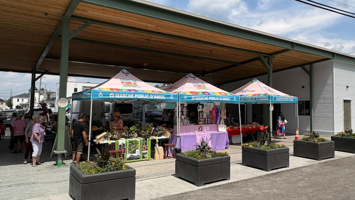 Protégés par un toit, des producteurs et des artisans reçoivent les clients au marché public.
