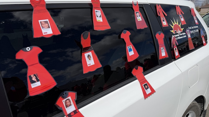 Sur un véhicule du centre de santé de la Première Nation, des cartons de robes rouges sont collés sur lesquels des photos et noms de personnes disparues sont apposées.